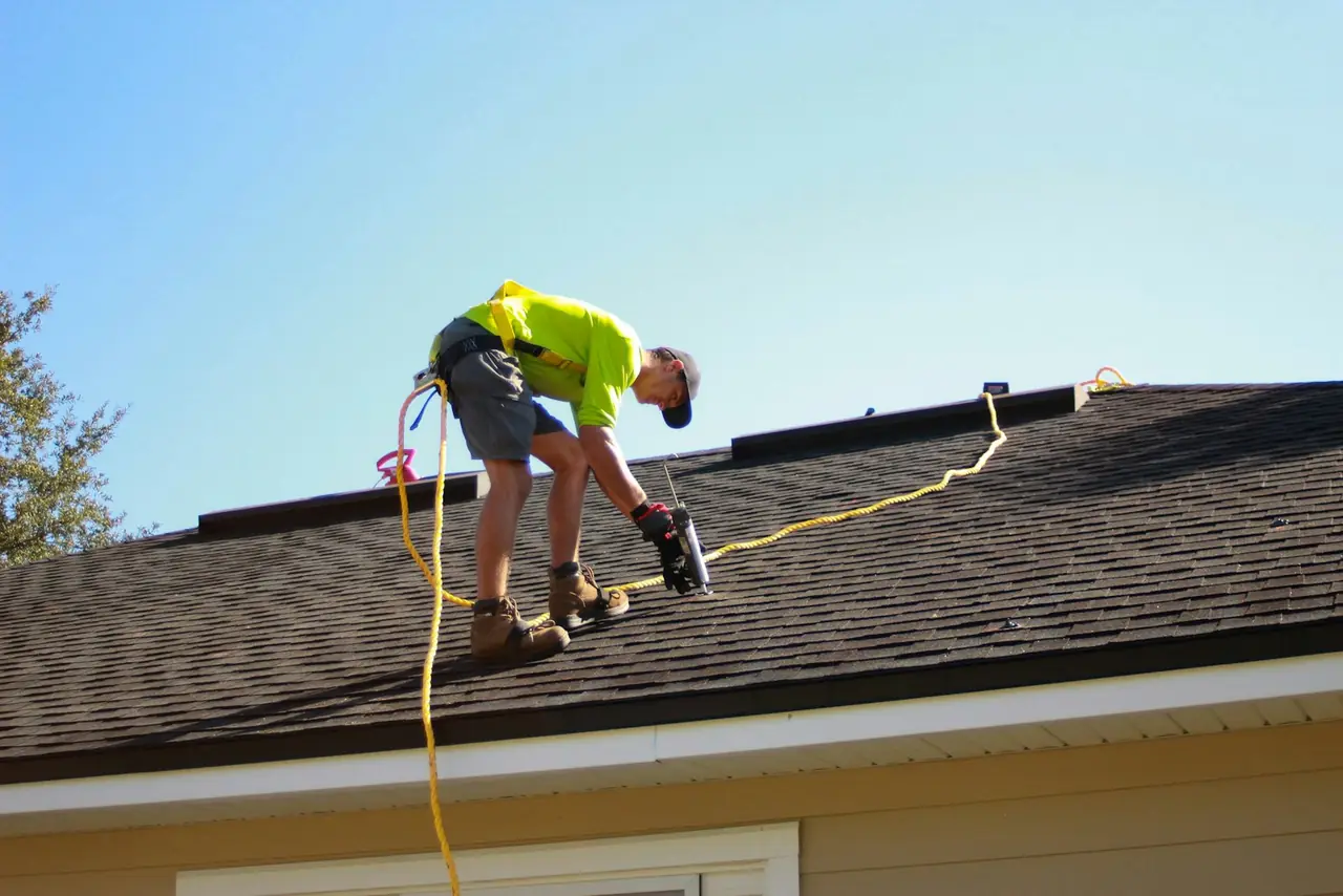 A roofer fastening shingles on a roof under a blue sky